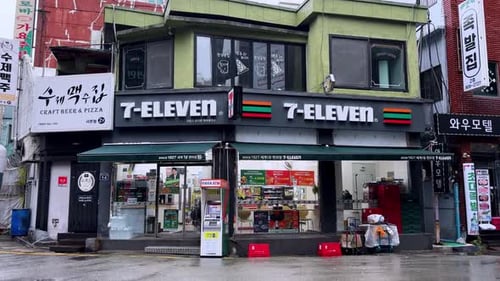 Boutique 7-Eleven au coin d'une rue pluvieuse à Busan avec les boutiques environnantes en vue