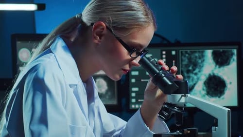 Female Scientist Looks Through Microscope in Laboratory