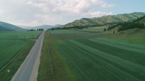 Aerial View of an Asphalt Road in Rural Area Between Green Fields and Hills