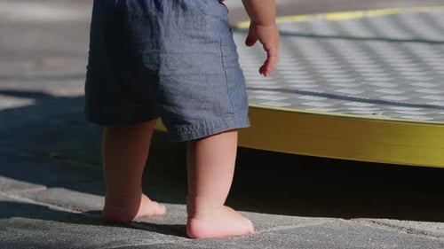 Barefoot toddler reaching toward playground merry go round then losing balance and falling to