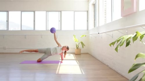 Young Caucasian woman performs a side plank exercise with a purple ball, with copy space