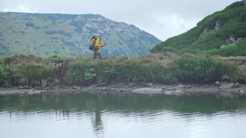 A tourist with a backpack walks through the mountains near the lake