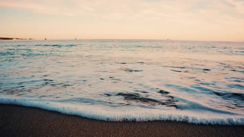 Close up of small ocean waves gently rolling onto the sandy beach at sunset