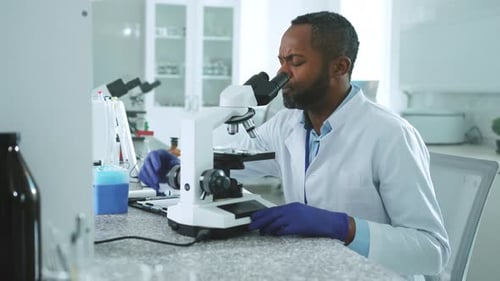 Close Up Serious Handsome African American Scientist Man in Uniform Looking Under a Microscope