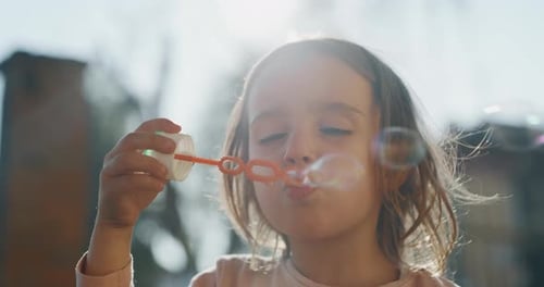 Authentic close up shot of little girl blowing soap bubbles in spring park on a sunny day.