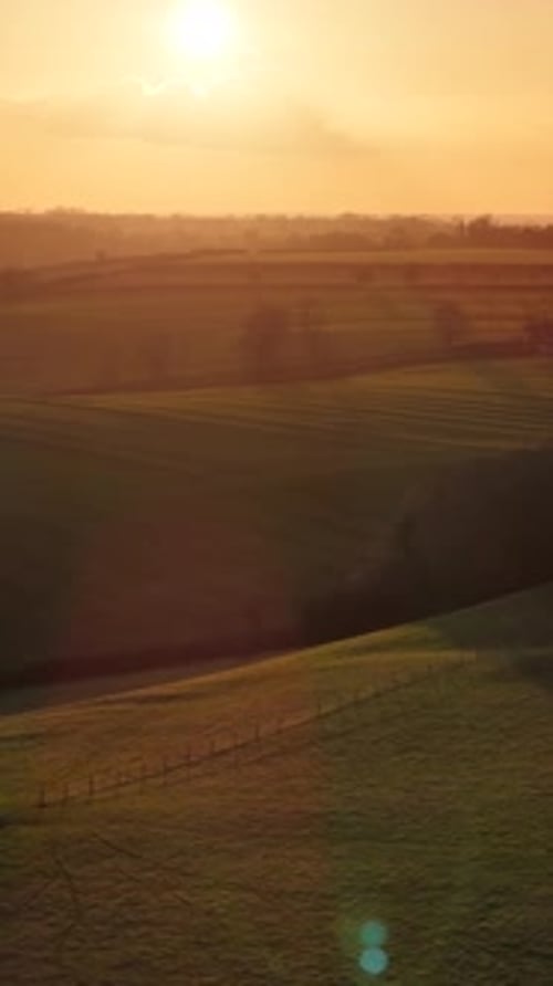 Vidéo verticale : une lumière dorée se répand sur de vastes collines, des terres agricoles idylliques et des collines vallonnées