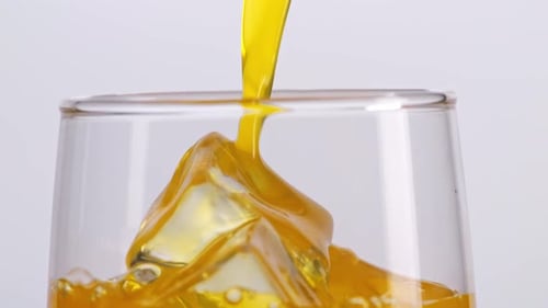 Close Up Of Orange Juice Being Poured Into A Glass With Ice Cubes On White Background