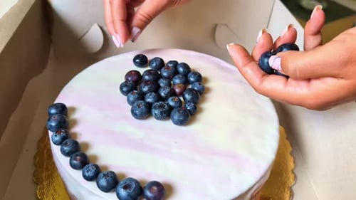 Hands Decorating Cake with Blueberries in a Box