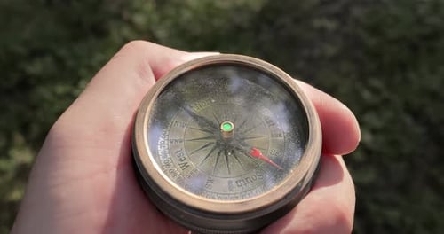 Traveler hand holds a old directional compass in summer forest. Person use compass to find location.
