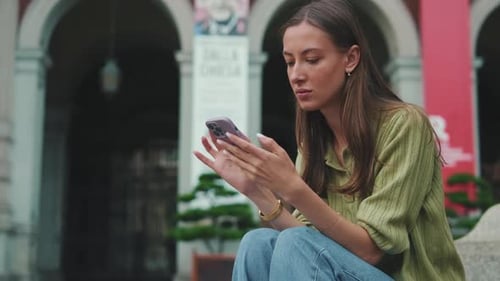 Young woman uses a phone while sitting on the square of the old city