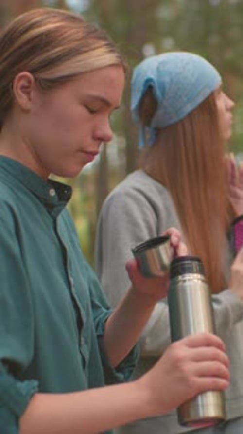 Hikers Enjoy Relaxing Moment in Forest with Thermos and Hair Care