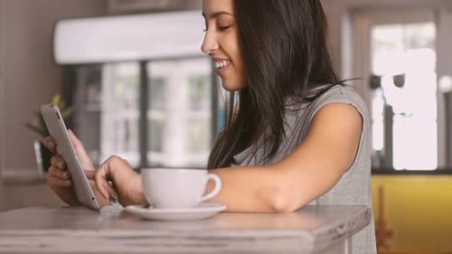 Woman uses tablet, cafe setting, with coffee