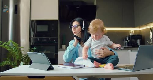 Madre trabajando en el ordenador portátil y hablando en el ordenador portátil Comunicación por vídeo con sus parejas mientras el bebé juega