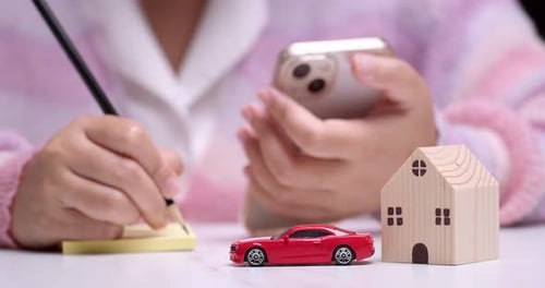 Close-up of an individual calculating finances on her car and house loans using a pencil, paper, and
