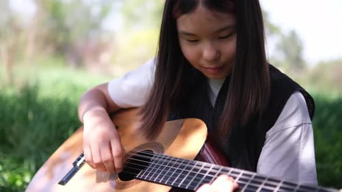 Young Girl Plays Guitar Outdoors in the Grass