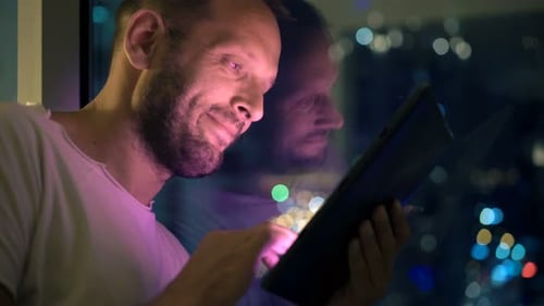 Young Man Using Tablet Computer Standing by Window at Home at Night Adult