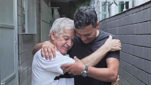 Senior Father And Son Hugging Each Other And Facing Camera With Bright Smiles In Serene Outdoor