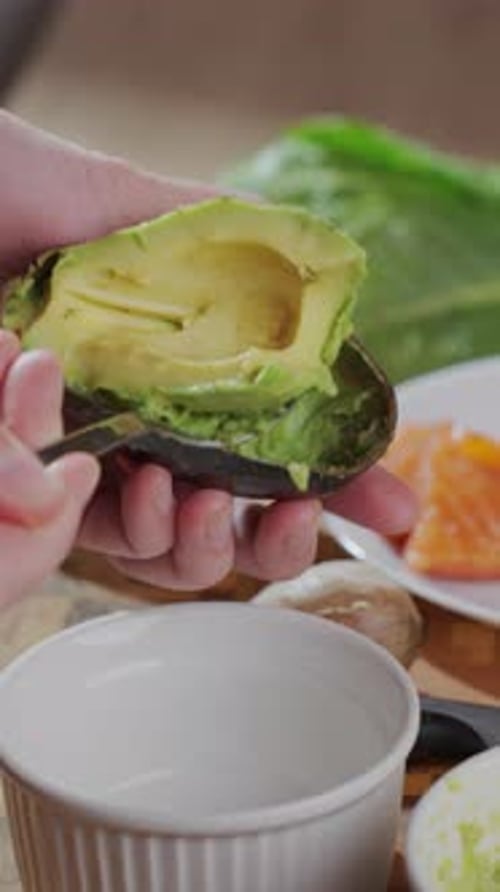 Hands Scooping Avocado Into Ramekin on Wooden Cutting Board Close Up