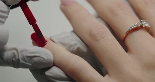 Manicure Master Hands in Gloves Applying Red Gel Polish on Client Nail