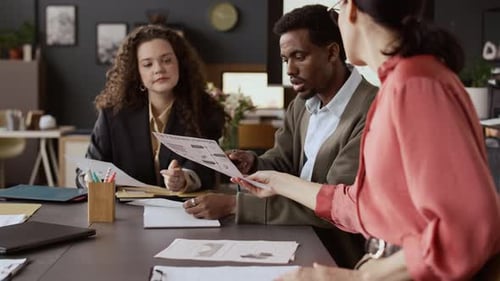 Coworkers Gathering to Discuss Report at Desk in Office