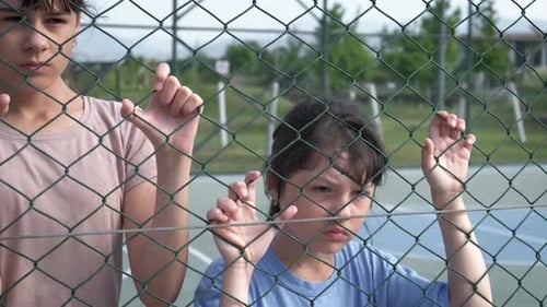 Two Sad Children Behind Chain Link Fence
