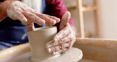 Mains d'un potier biracial à longue barbe travaillant sur un vase en argile dans un atelier de poterie, au ralenti
