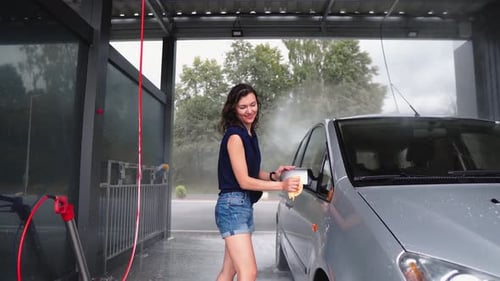 A Young Woman is Happily Washing Her Car at a Selfservice Car Wash on a Sunny Day Showing Her Care
