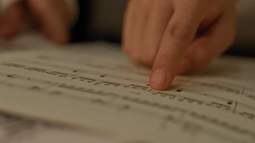 De cerca de los dedos de las niñas siguiendo la anotación en el libro de partituras musicales.