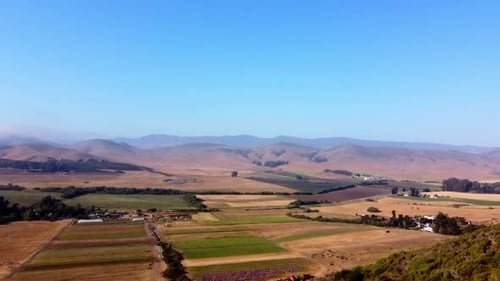 Drone shot over farm with hills and blue sky in the background.