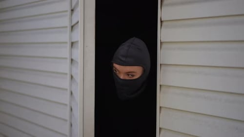 Jeune cambrioleuse masquée jetant un coup d'œil par la porte du garage avec un regard prudent