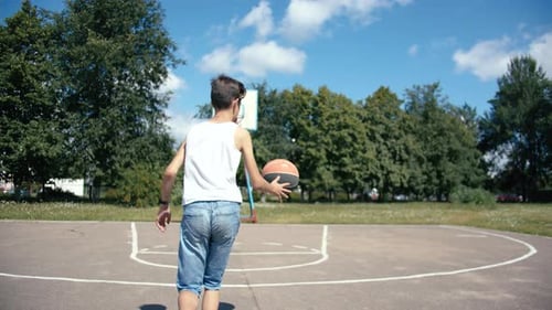 Boy Dribbles and Shoots Basketball Outdoors on Sunny Day