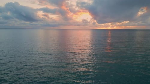 Golden sun rays breaking through grey clouds over dark ocean at sunset