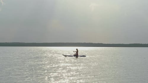 Silhouette of Young Female Paddle Boarding at Sunset