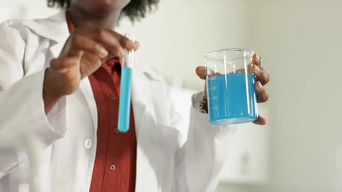 En soulevant le tube à essai, le scientifique stabilise le bécher et le tube tout en comparant le liquide bleu sur un banc