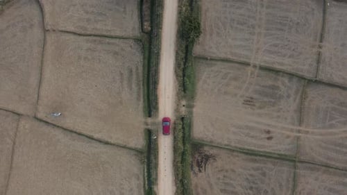 Red Car Driving on Rural Dirt Road Through Agricultural Fields, Karnataka, India.