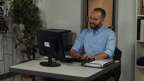 Happy male office worker, types on keyboard