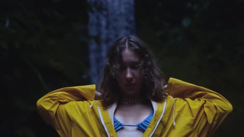 Woman Puts Hood on Raincoat near Waterfall