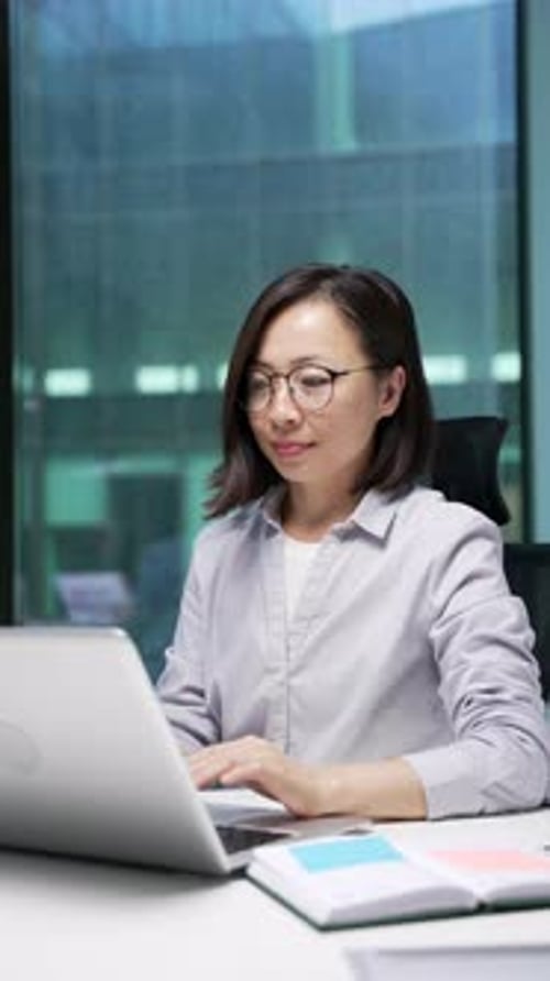 Asian businesswoman typing on laptop computer sitting at desk at workplace in business office.