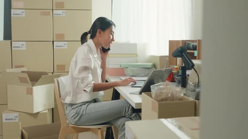 Woman Working at Table Surrounded by Boxes