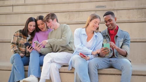 Friends Laughing While Looking at Cell Phones Together