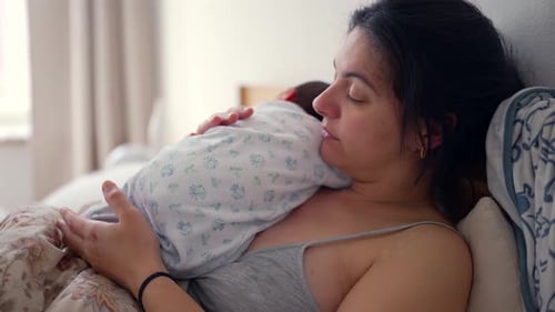 New Mother Cradling Newborn Baby in Bed