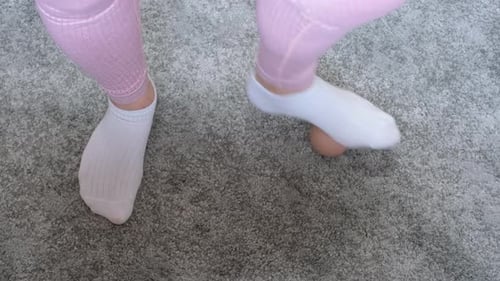 A woman's foot in white socks rolls a massage ball on gray carpet, top view.