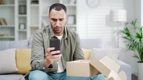 Young Adult Using Phone Next to Unopened Box