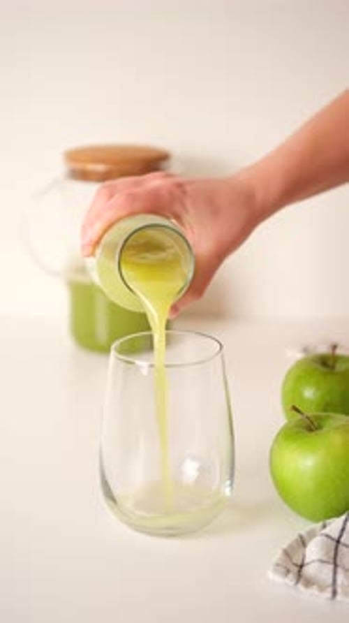 Hand Pouring Green Juice into a Glass