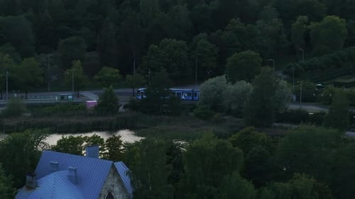 Aerial View of Streetcar Passing Around Cars on Street in Town Outskirts Trees in Parks After Sunset