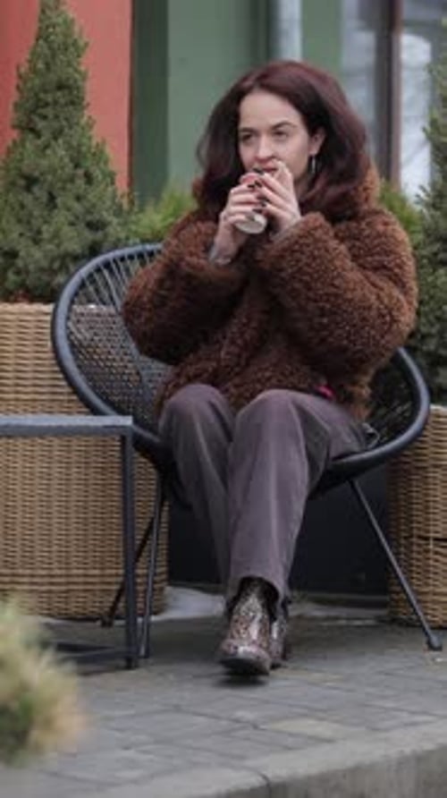 Young Woman in Fur Coat Drinks Coffee Outside