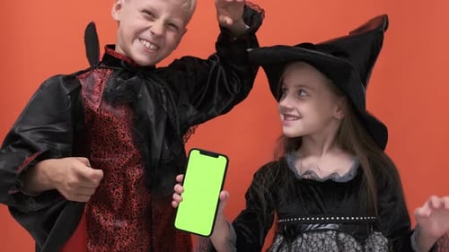 Smiling Children in Halloween Costumes Hold Green Screen Phone
