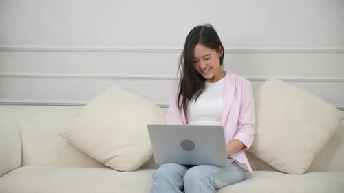 Young Woman Smiling, Using Laptop on Couch Indoors