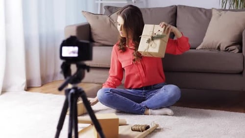 Alegre vloguera hispana graba un vídeo tutorial para envolver regalos de Navidad en casa