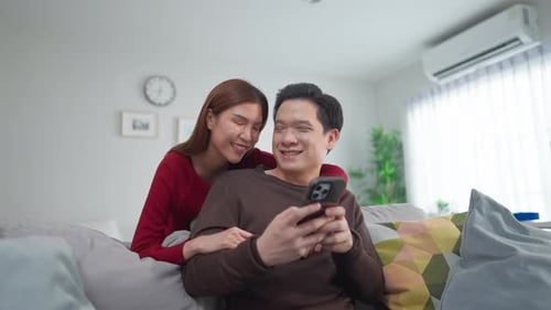 Happy Couple Using Mobile Phone on Couch at Home